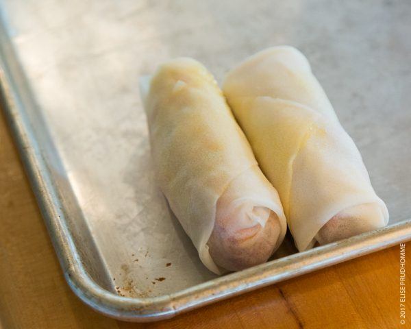 Completed shrimp rolls on a metal tray ready to be cooked or frozen.